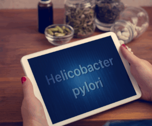 Tablet z napisem „Helicobacter pylori”, na stole w tle widoczne naturalne suplementy i zioła wspierające leczenie infekcji H. pylori.